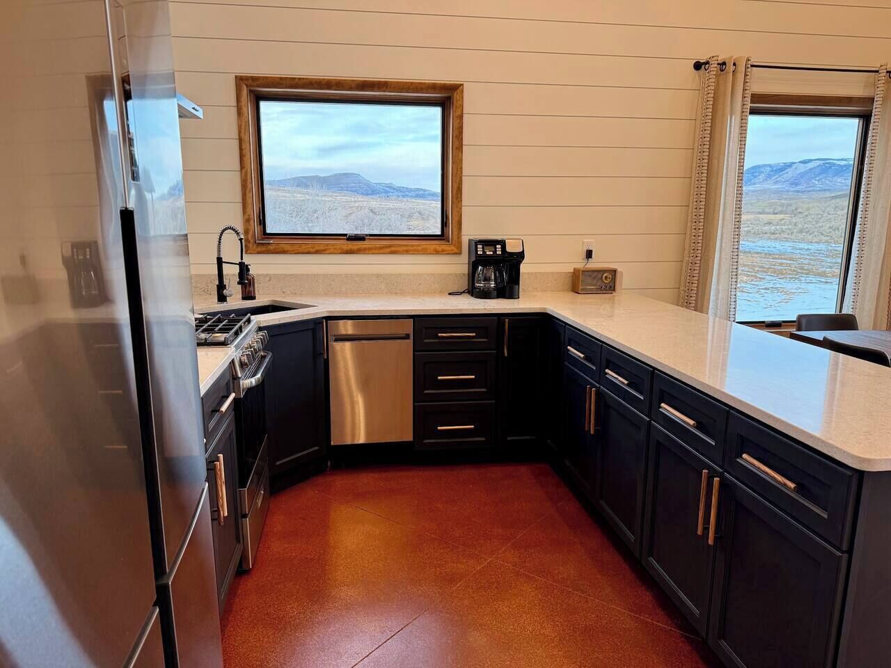 Una cocina compacta con refrigerador de acero inoxidable, horno integrado, cafetera y ventana con vista a un paisaje montañoso.
