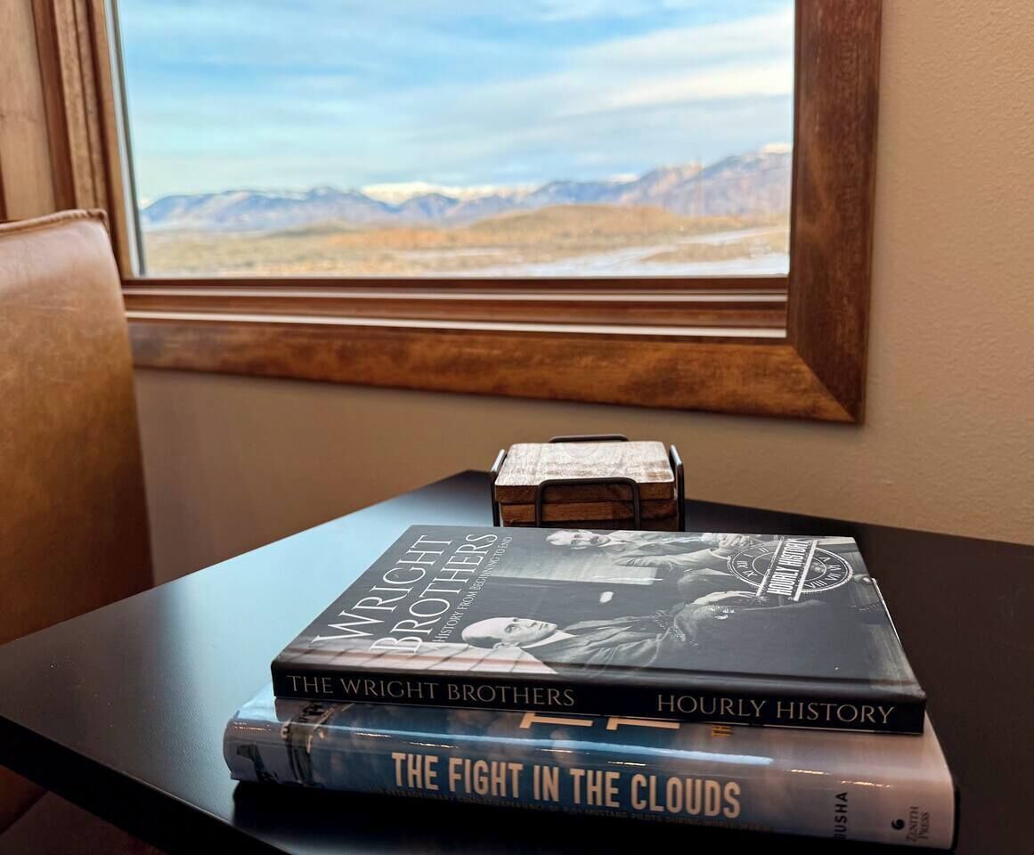 A stack of books on a table near a window with a mountain view.