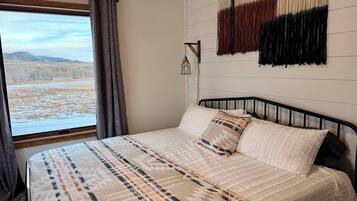 Een slaapkamer met een bed, een raam met gordijnen en een wandlamp.
