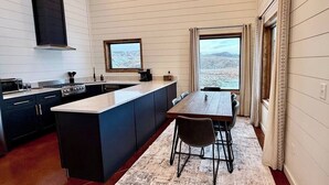 Cozinha moderna com uma ilha grande, armários escuros e vista para as montanhas pelas janelas.