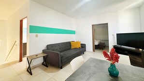 A modern living room with a sofa, a coffee table, a TV, and a vase with red flowers. - Vacation Getaway in Ocean Park With Parking (San Juan)
