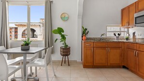 A modern kitchen with wooden cabinets, a granite countertop, and a dining area with white chairs and a table. - Vacation Getaway in Ocean Park With Parking (San Juan)