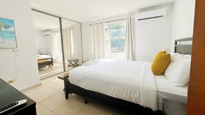 A hotel room with a bed, a desk, a chair, a window, and an air conditioning unit. - Vacation Getaway in Ocean Park With Parking (San Juan)
