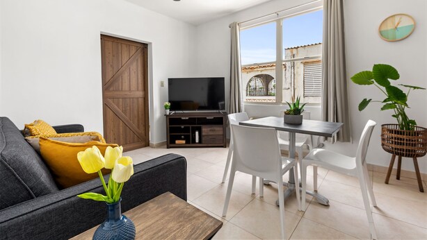 A living room with a sofa, TV, dining table, chairs, and a plant. - Vacation Getaway in Ocean Park With Parking (San Juan)