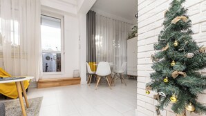 Un salón moderno con pared de ladrillo blanco, una zona de comedor con sillas blancas y un árbol de Navidad con adornos dorados.