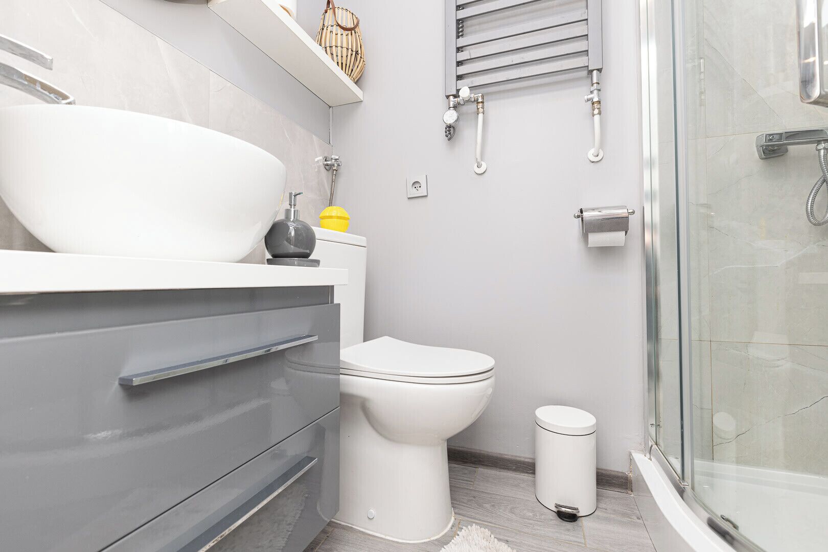 Un baño moderno con un lavamanos blanco grande, un inodoro, una cabina de ducha de vidrio y un pequeño cubo de basura.
