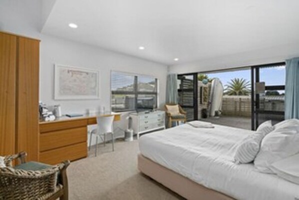 A bedroom with a bed, a desk, and a chair. There is a window with a view of the outside.