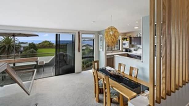 A modern kitchen with a large island, a dining area with a table and chairs, and a view of the outdoors through glass doors.