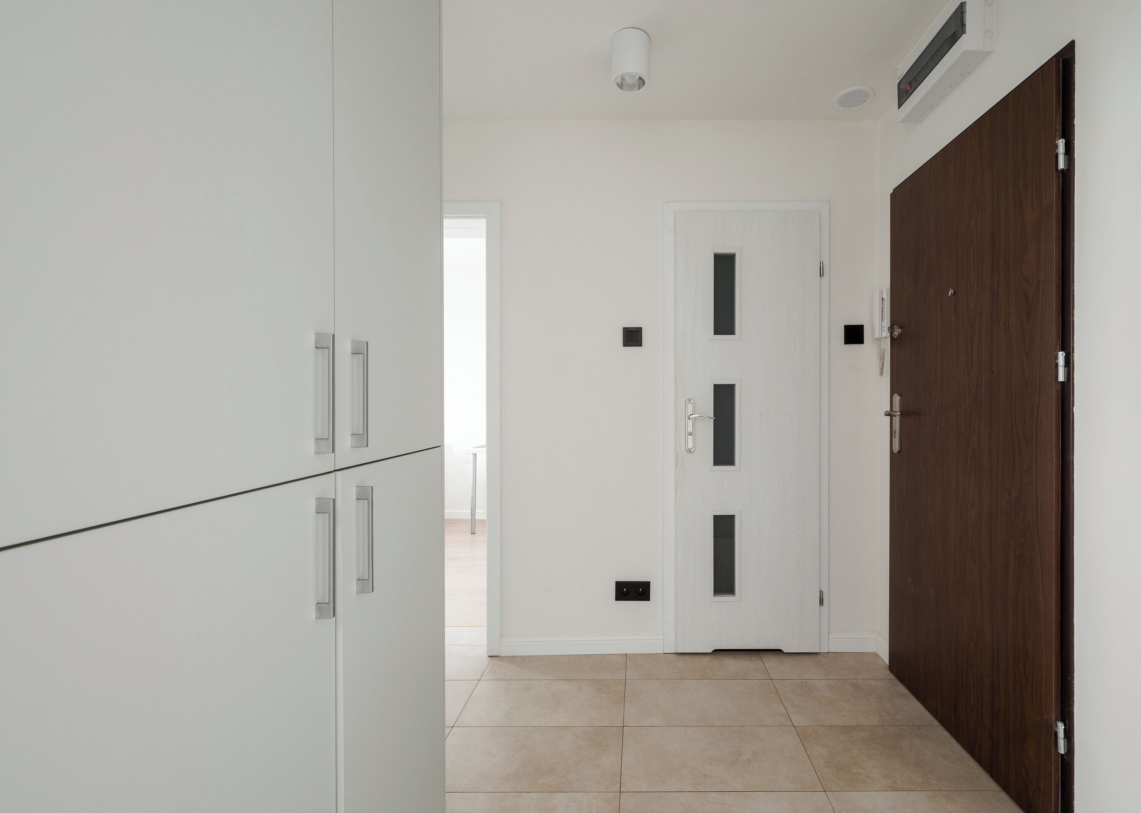 A hallway with white cabinets, a wooden door, and a tiled floor.