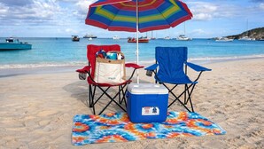 A beach scene with two beach chairs, a colorful umbrella, and a cooler on a towel.