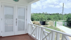 A balcony with white railings, a "Welcome" sign, and a view of a green landscape with a fence and trees.