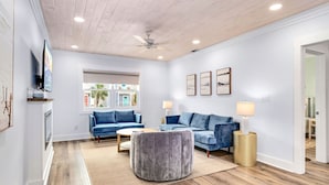 Un salon moderne avec un plafond en bois, deux canapés bleus, un pouf gris et une petite table ronde.