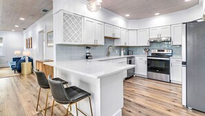 Une cuisine moderne avec des meubles blancs, un îlot central, des appareils en acier inoxydable et un plancher en bois.