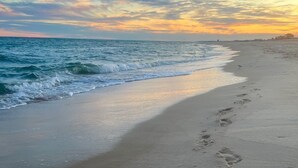 Une plage où l’on voit des empreintes de pas menant à l’eau, un ciel dégagé et un horizon lointain.