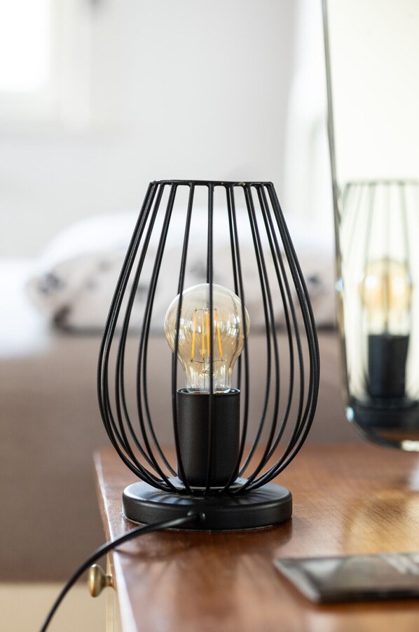Une lampe moderne dotée d’un abat-jour en verre transparent et d’un pied en fil de fer noir, posée sur une surface en bois.