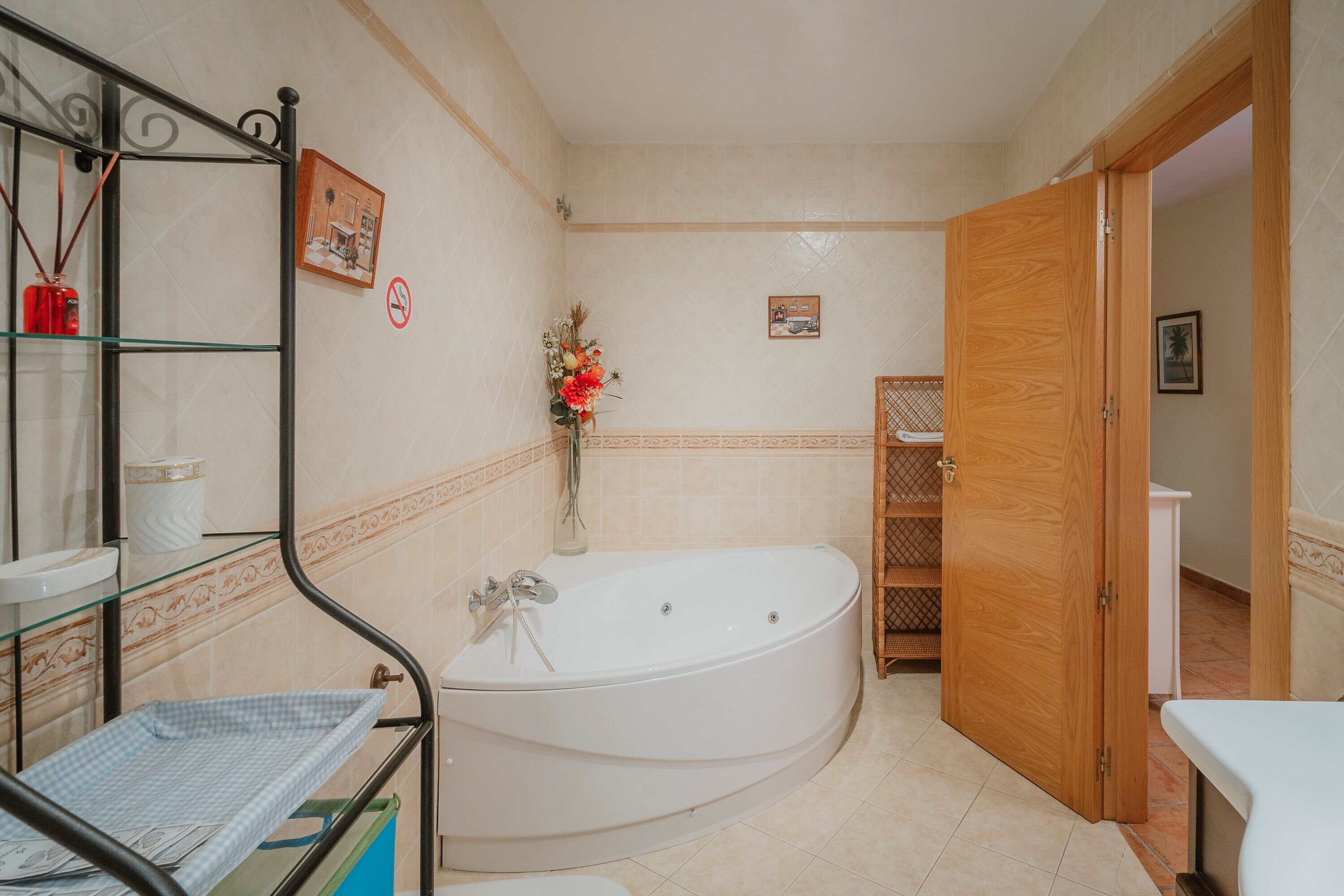 Een badkamer met een badkuip, een glazen plank met toiletartikelen, een houten deur en een betegelde vloer.