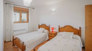 A bedroom with two wooden beds, a nightstand with a lamp, a window with curtains, and a radiator.