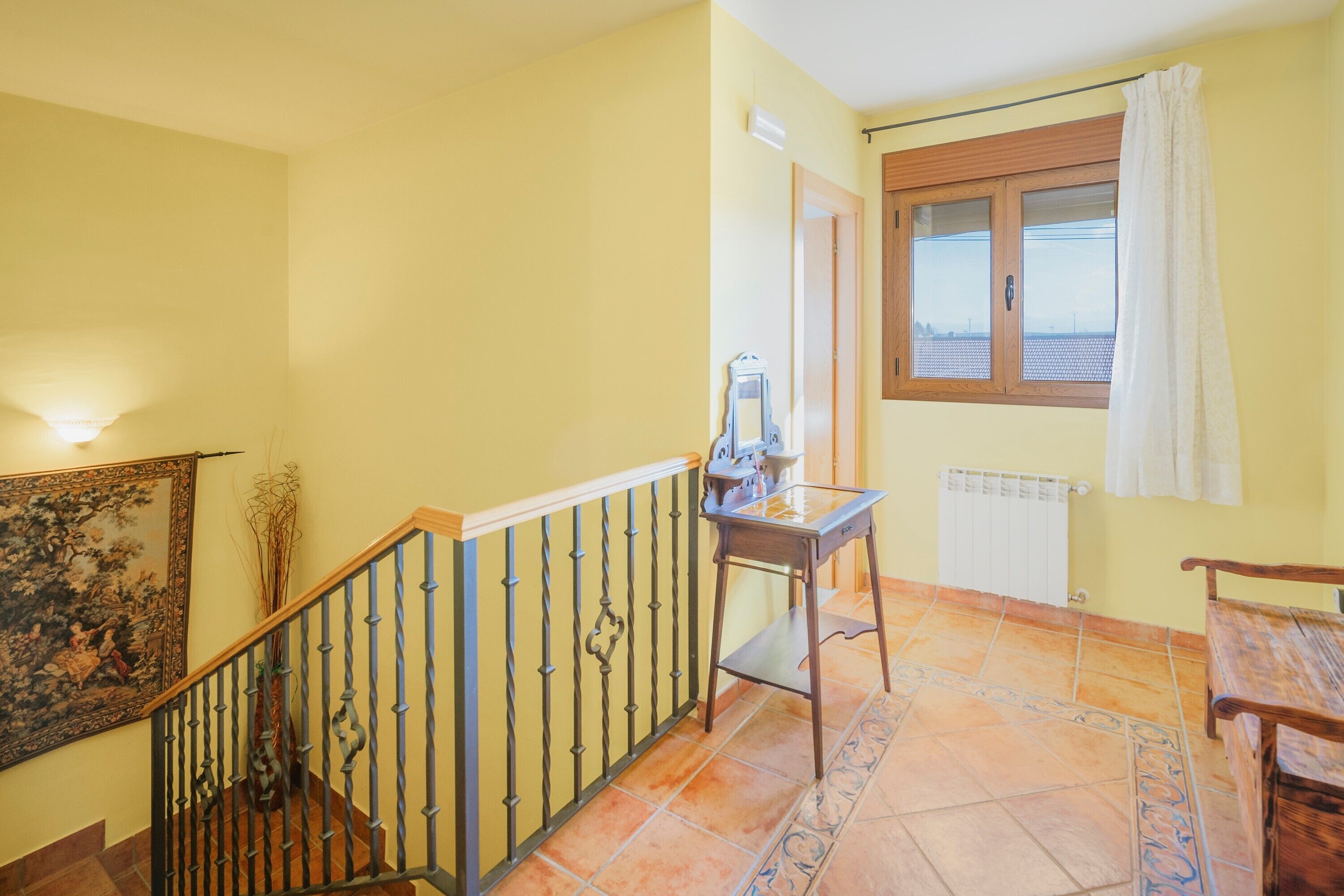 A staircase with a metal railing, a table with a vase, a radiator, and a window with a curtain.