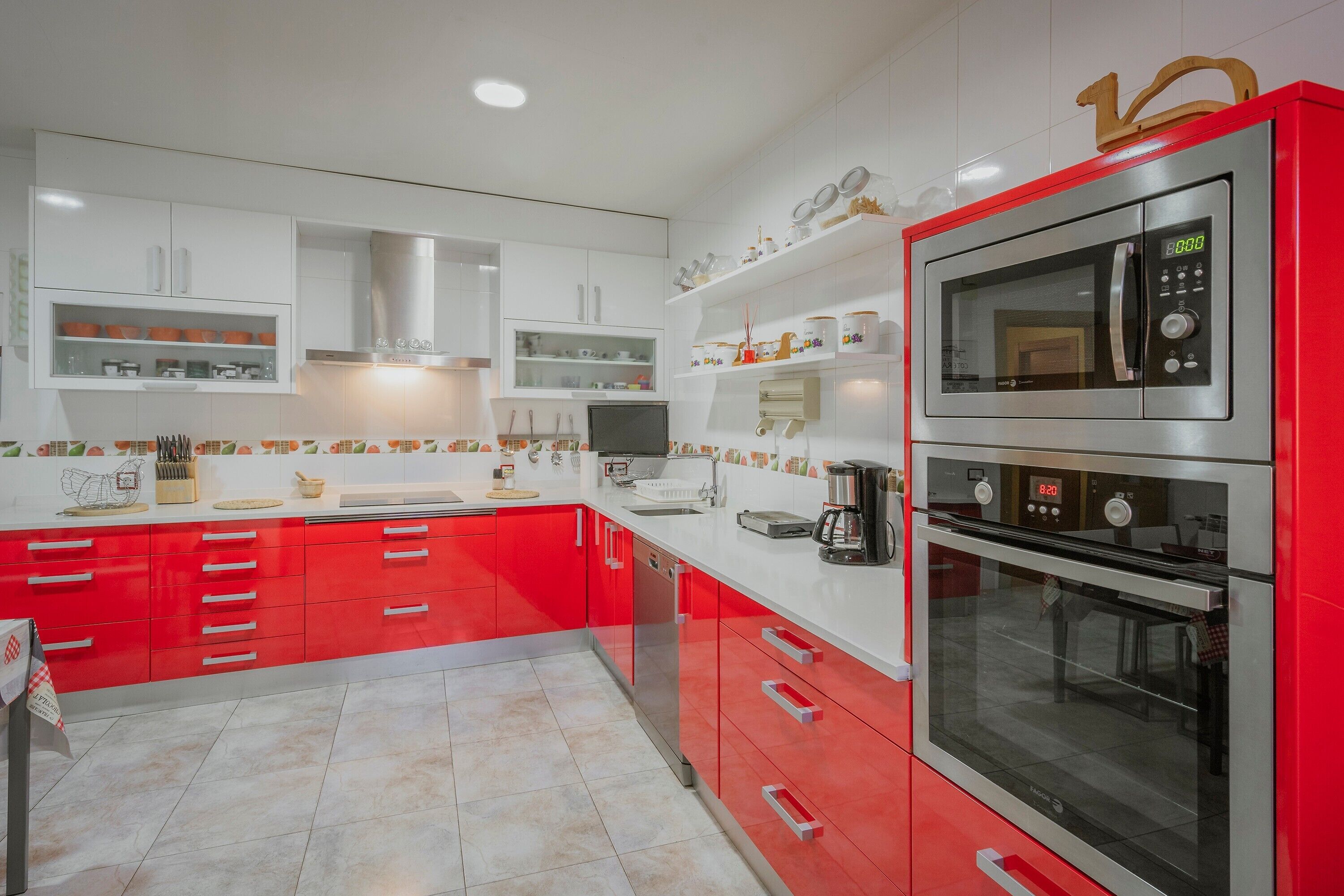 Una cocina moderna con muebles de cocina rojos y blancos, electrodomésticos de acero inoxidable y una distribución limpia y ordenada.