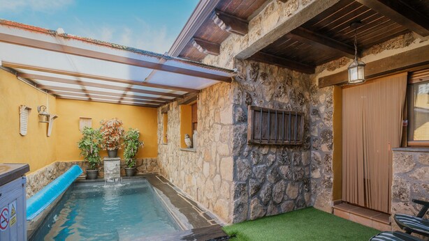 Une piscine bordée de pierres, avec un toboggan bleu, du gazon synthétique et une terrasse en bois.