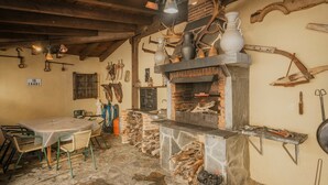 Une cuisine rustique avec une cheminée en pierre, des poutres en bois et un coin repas comprenant une table et des chaises.