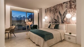 A bedroom with a large bed, a nightstand, a chair, a window with a view, and a wall with a floral pattern.