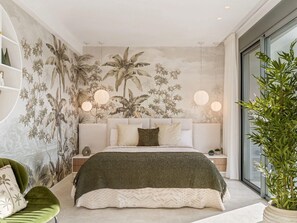 Un dormitorio moderno con una cama grande, una silla verde, una planta en maceta y un mural en la pared.