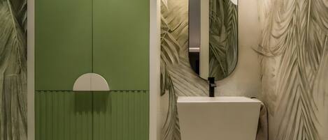 A bathroom with a green accent wall, a white sink, a mirror, and two wall-mounted lights.