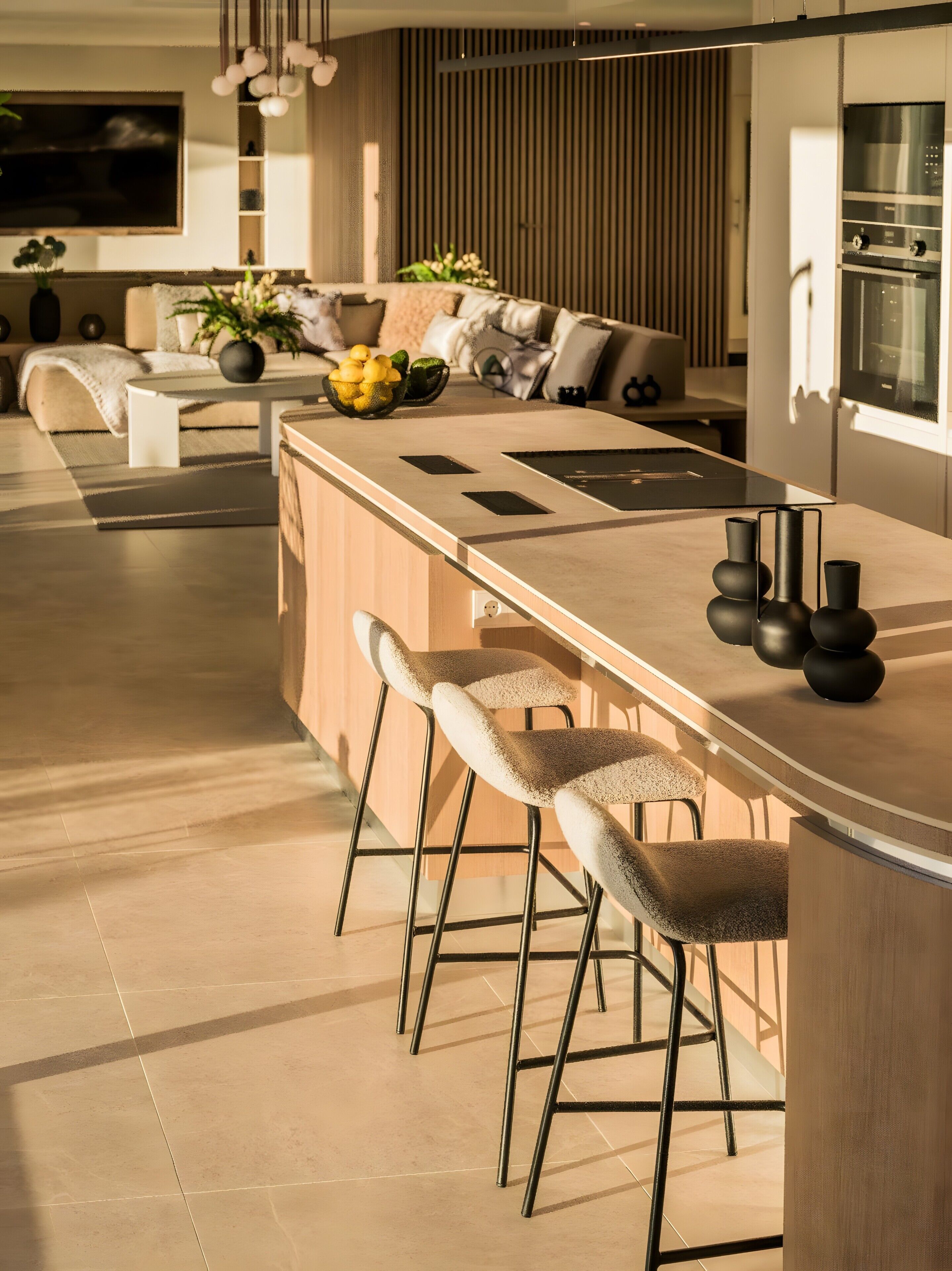 Cozinha moderna com ilha central, banquetas e área de refeições com sofá.