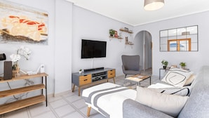 Un salon moderne avec un téléviseur à écran plat, un canapé gris, une table basse en bois et un tableau accroché au mur.