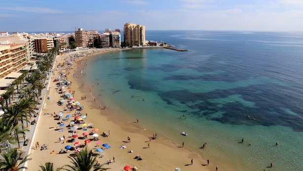 Une plage avec une eau cristalline, des palmiers et des bâtiments en arrière-plan.