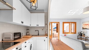 Une cuisine moderne avec des meubles blancs, un four à micro-ondes, un lave-linge et un plan de travail en bois.