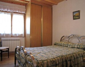Ein Schlafzimmer mit Bett, Stuhl, Heizkörper und einem Vorhangfenster.