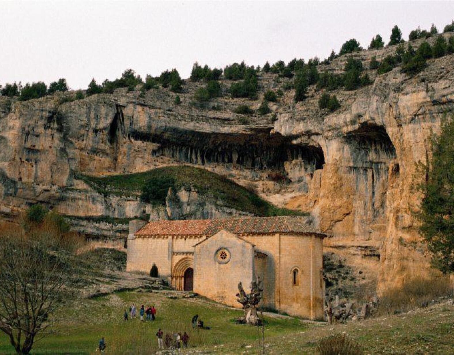 A small building with a tiled roof, situated in a rocky landscape with a few people around.