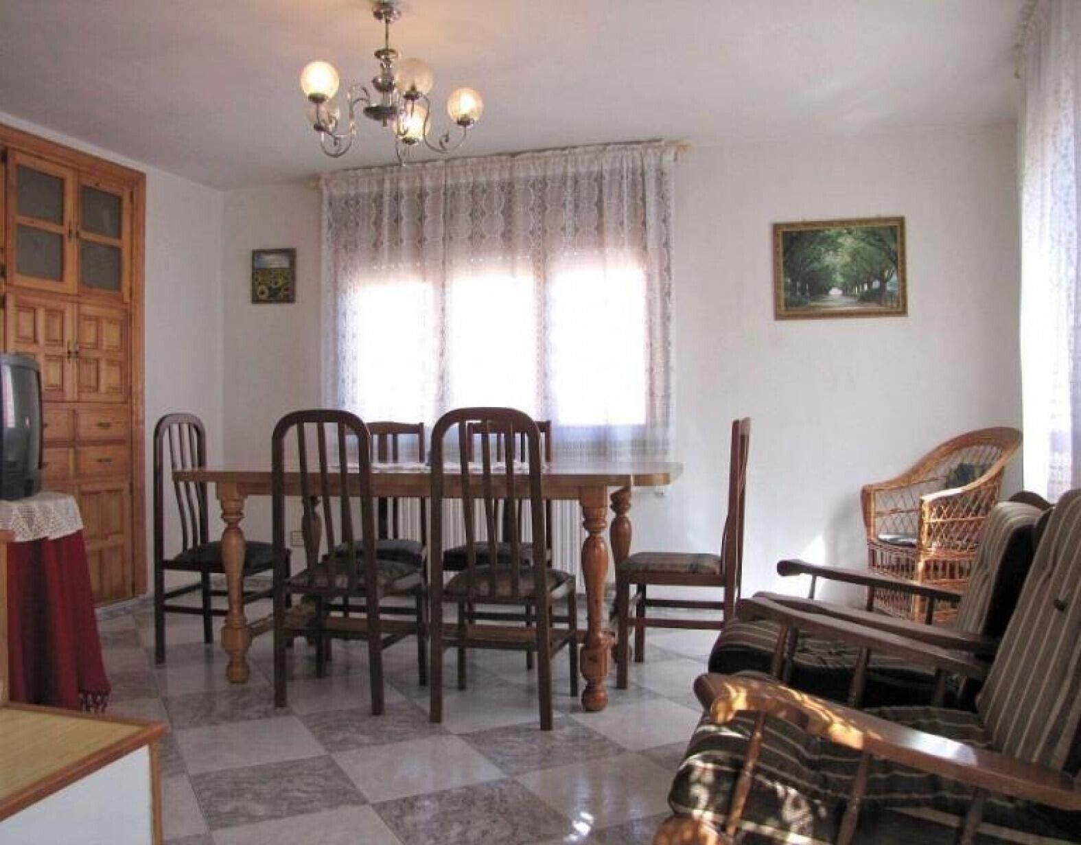 Un comedor con una mesa y sillas, una araña, un sofá y un televisor.