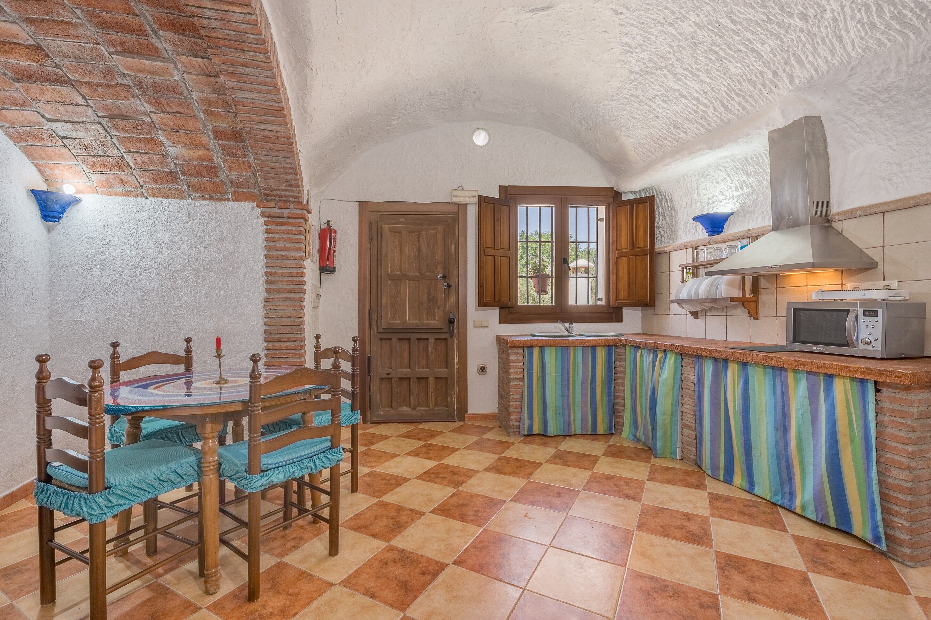 Une cuisine avec un carrelage à motifs, une table et des chaises en bois, un four à micro-ondes et une fenêtre avec des volets en bois.