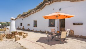 En hvid bygning med et tegltag, et bord med stole, en orange parasol og krukker med planter.