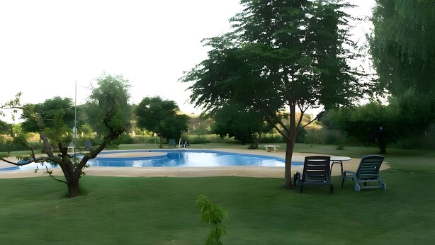 Una piscina rodeada de césped, árboles y mobiliario de exterior.