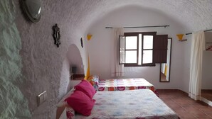 Un dormitorio con dos camas, una ventana con cortinas, un espejo y una lámpara fijada a la pared.