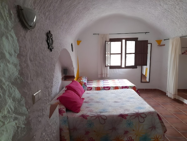 Ein Schlafzimmer mit zwei Betten, einem fensterbelaubten Fenster, einem Spiegel und einer Wandleuchte.