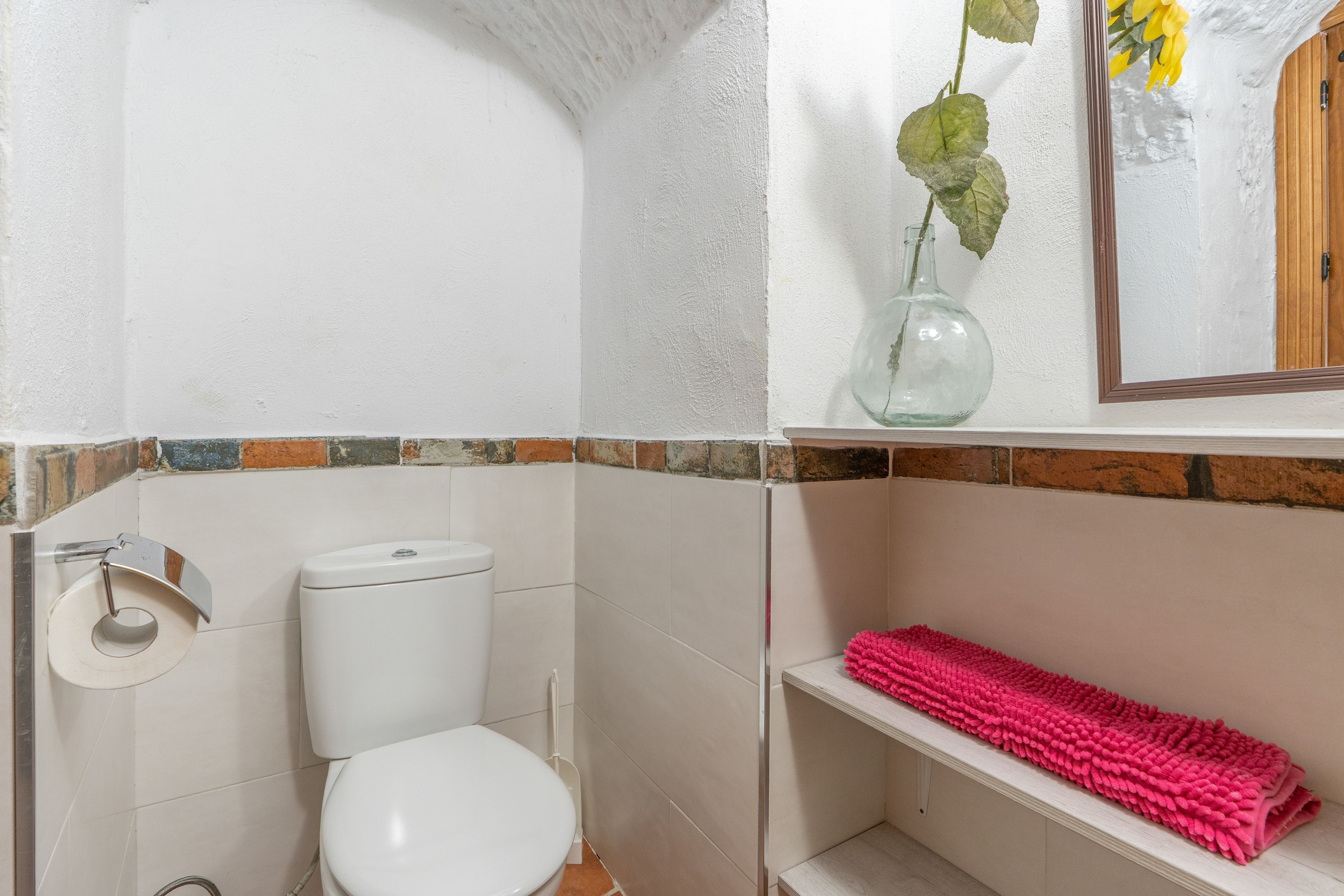Une salle de bain avec des toilettes, une étagère sur laquelle est posée une serviette rose et un vase avec une plante.