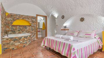 Una habitación con pared de ladrillo, una bañera blanca, una cama con ropa de cama a rayas y un techo blanco con textura.