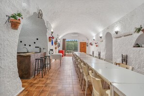 An interior with a long dining table, chairs, a kitchen area, and a view through an open door. - Country House 'El Melocotonero' with Mountain View, Wi-Fi and Air Conditioning (Benalúa)