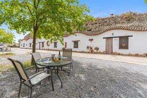 An outdoor seating area with a table set for two, surrounded by chairs, in front of a white building with a tiled roof. - Country House 'El Melocotonero' with Mountain View, Wi-Fi and Air Conditioning (Benalúa)