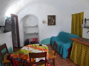 Ein gemütliches Zimmer mit einem runden Tisch, Stühlen, einer Couch, einem Fernseher und einem Bild an der Wand.