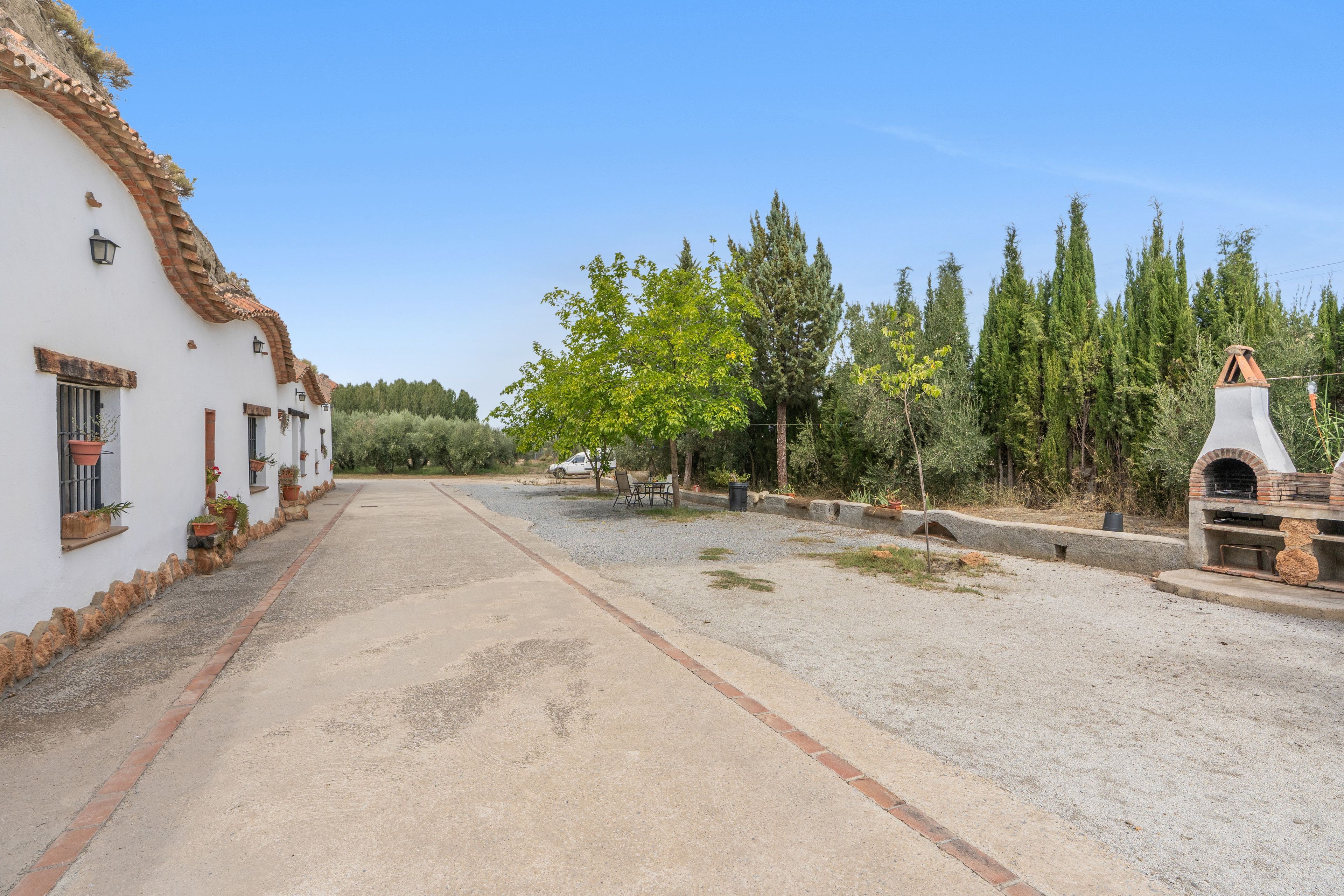 Una propiedad rural con camino de grava, un edificio blanco con techo de tejas y una estructura de horno de ladrillo.