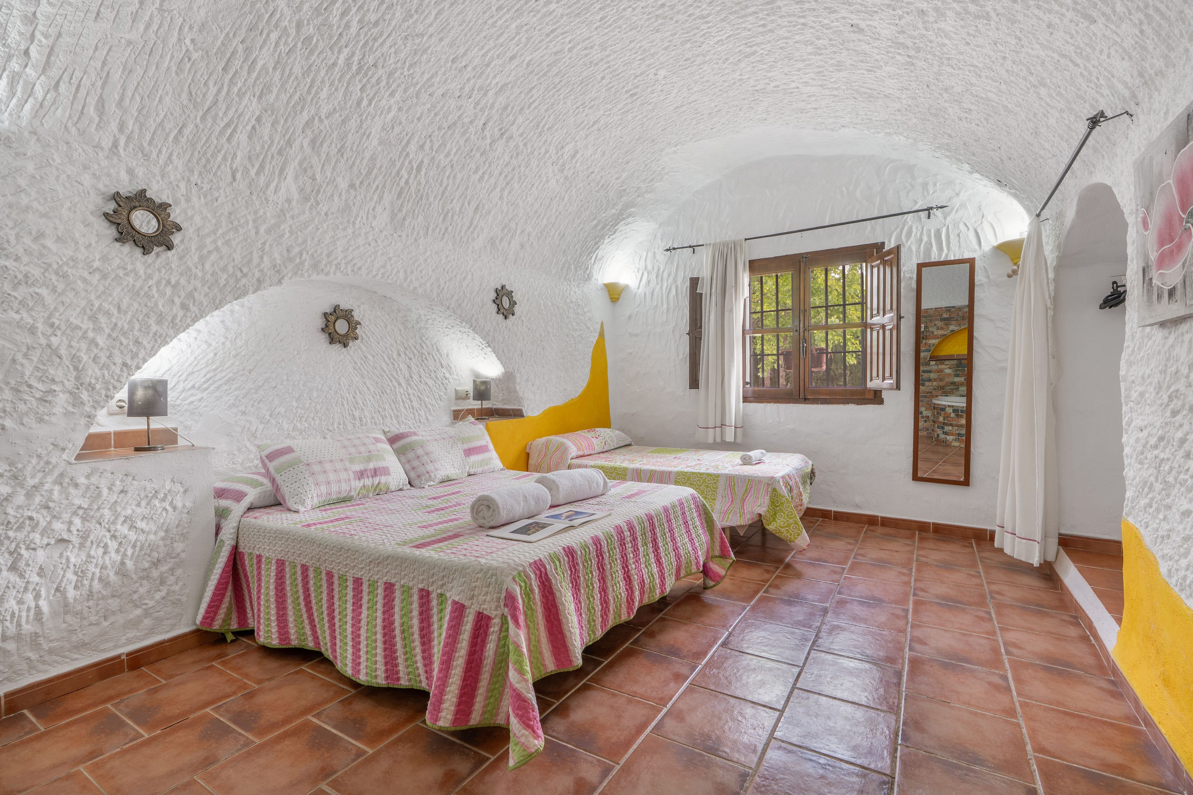 Een gezellige slaapkamer met twee bedden, een raam met gordijnen en een rustieke stenen muur.