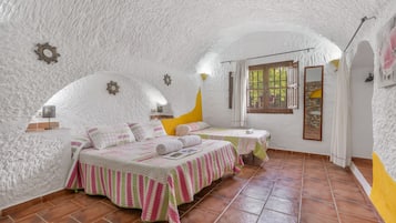 Een gezellige slaapkamer met twee bedden, een raam met gordijnen en een rustieke stenen muur.