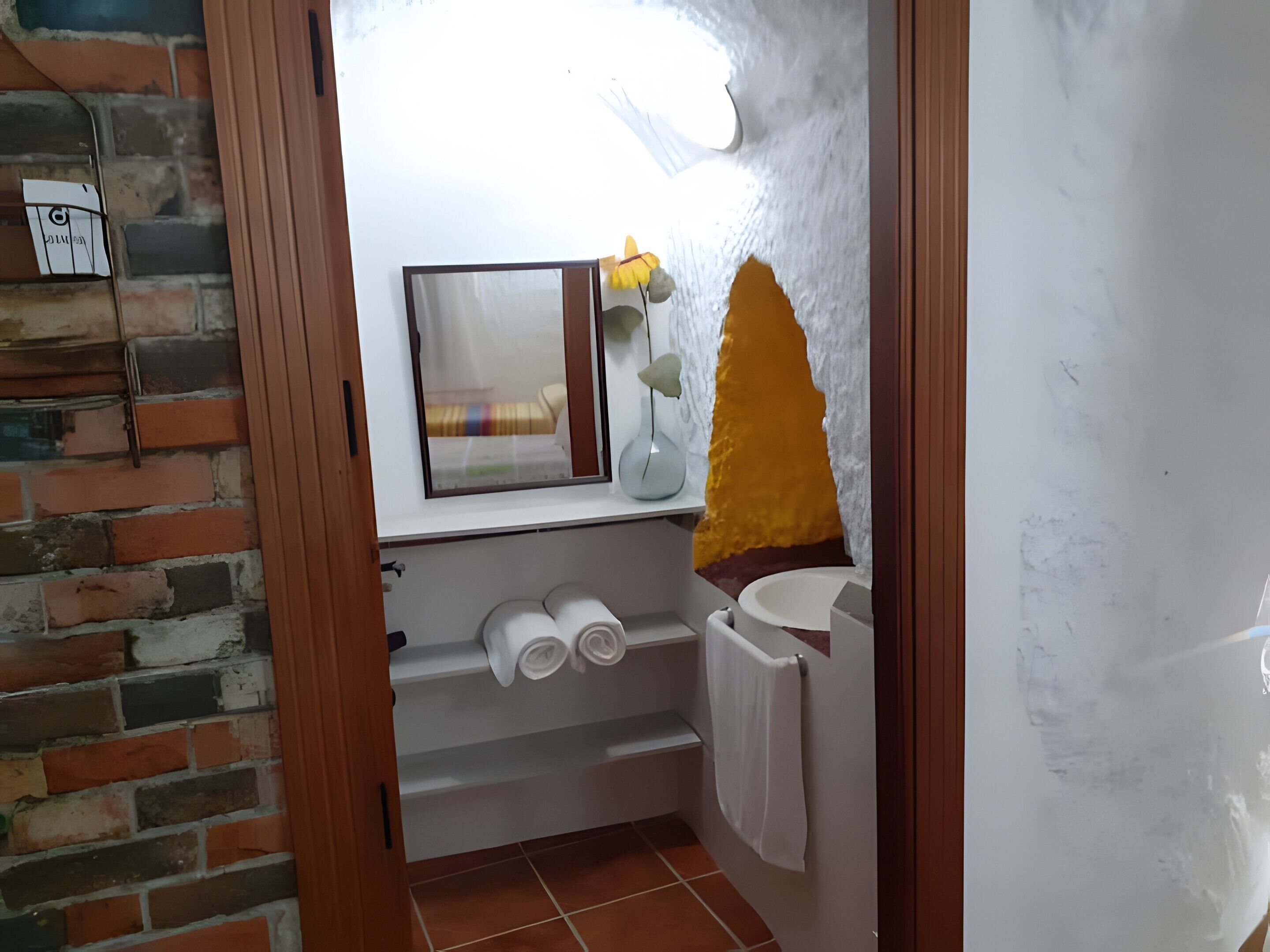 A bathroom with a brick wall, a window with a view, a towel rack, and a toilet.