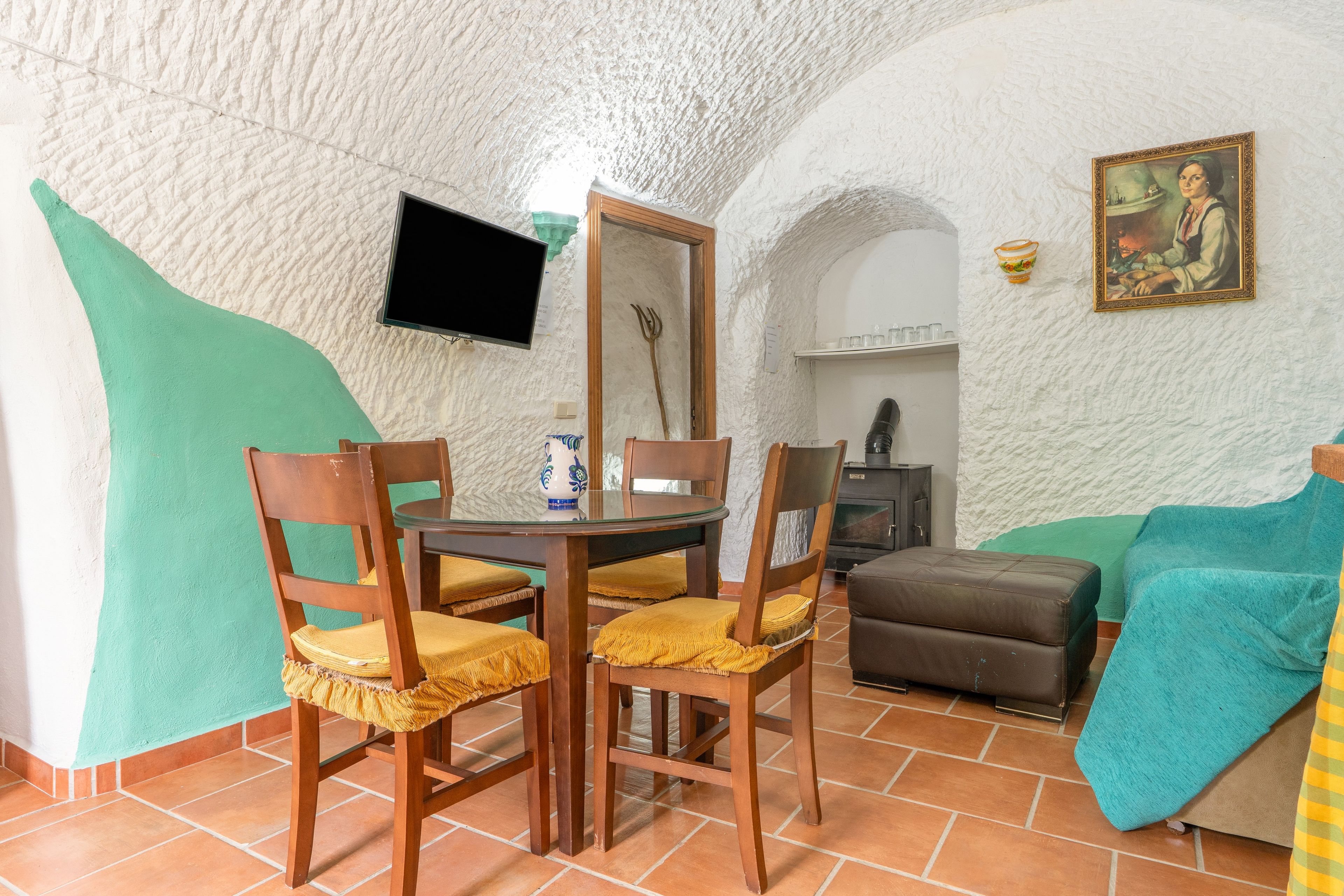 A cozy room with a round dining table, wooden chairs, a sofa, and a television mounted on the wall.